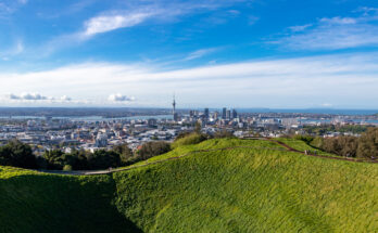 Panoramablick von einem grünen Vulkankrater auf die Skyline von Auckland und den Hafen.