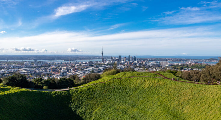 Panoramablick von einem grünen Vulkankrater auf die Skyline von Auckland und den Hafen.