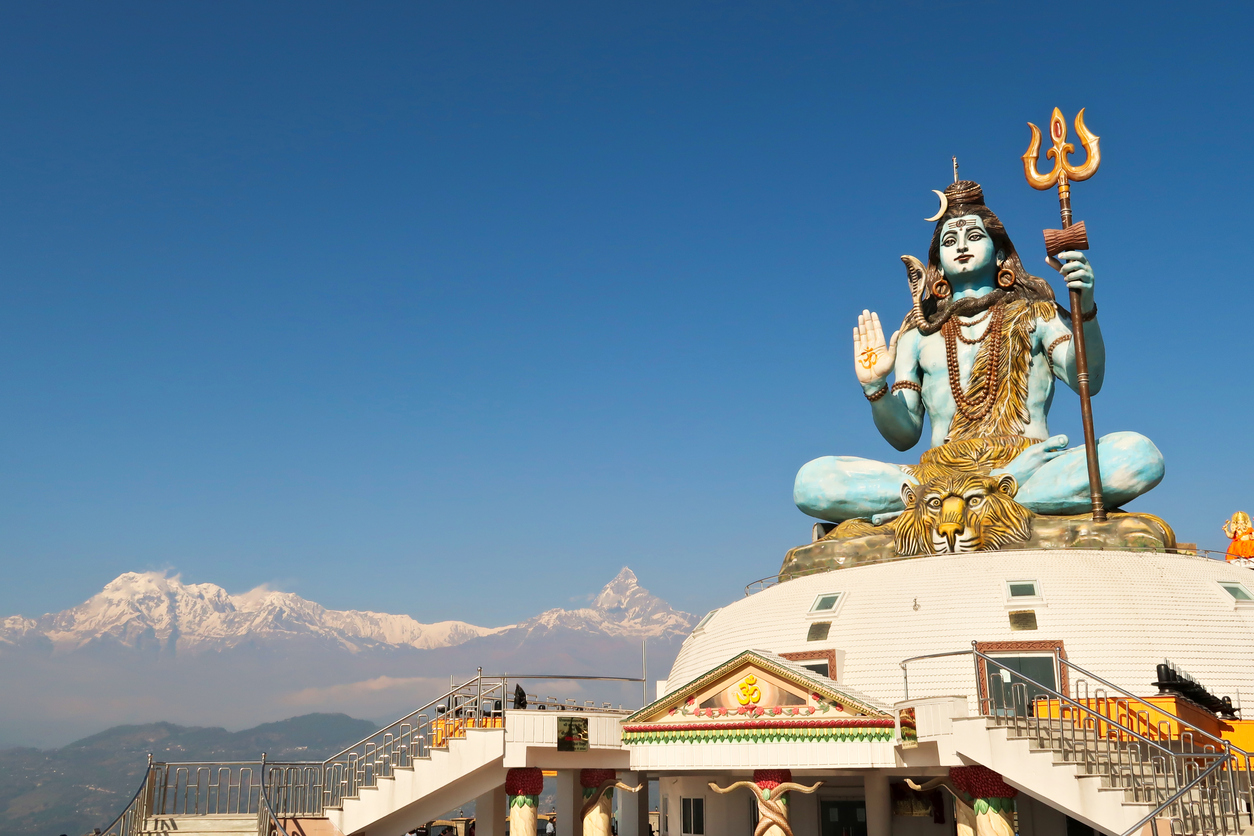 Riesige blaue Shiva-Statue auf einem Tempel in Pokhara mit schneebedeckten Himalaya-Gipfeln im Hintergrund.