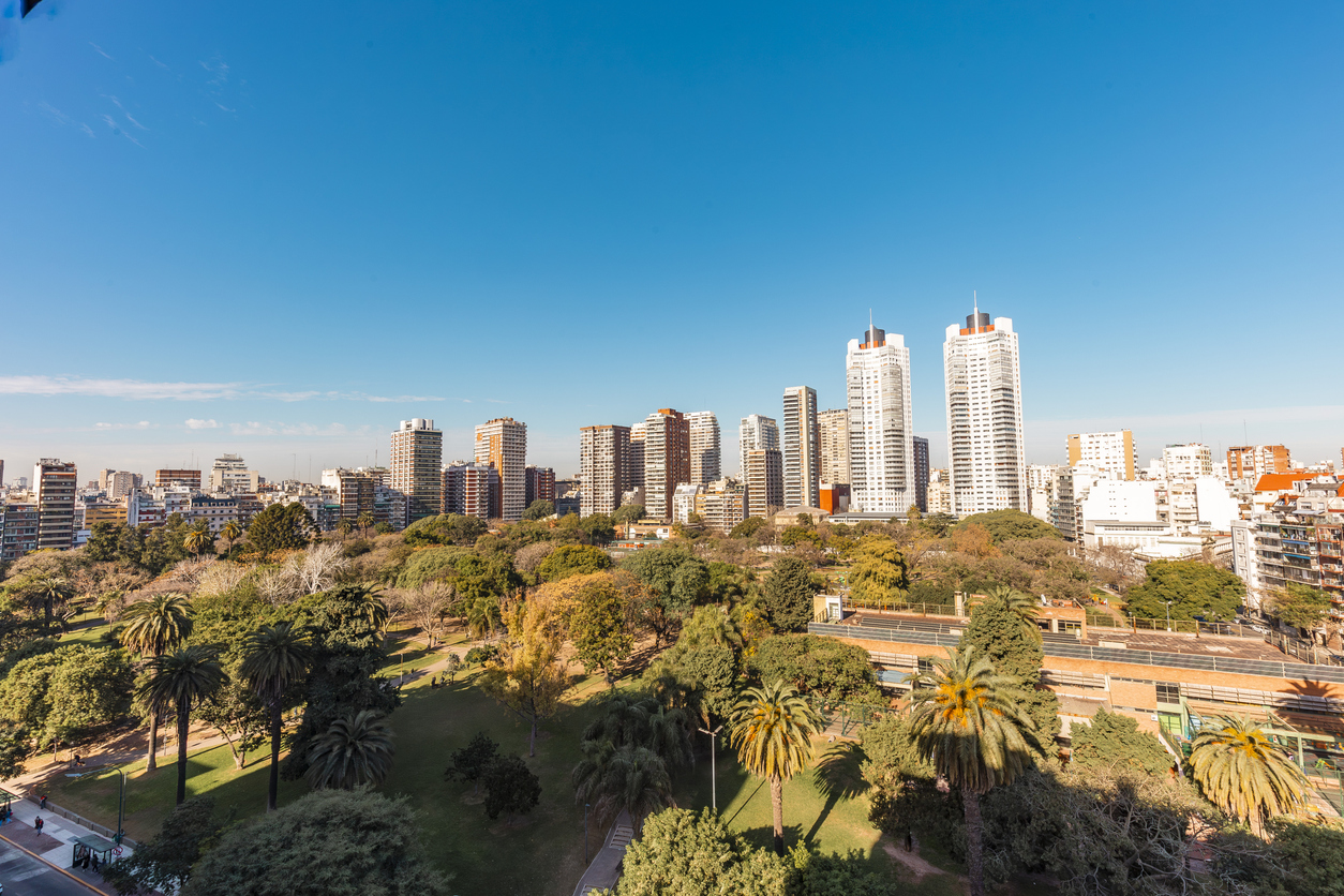 Hohe Wohn- und Bürohäuser hinter einem großen Park in Buenos Aires bei klarem Himmel.