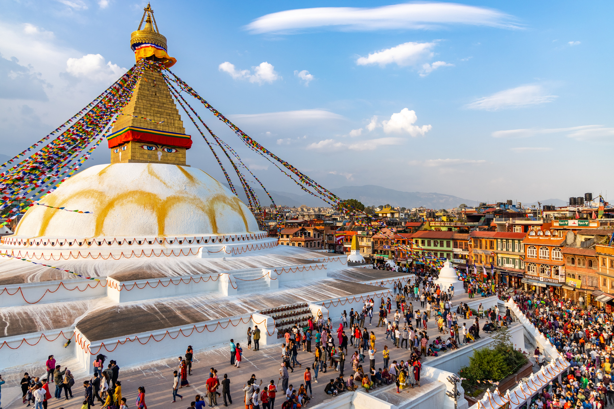 Der große Boudhanath Stupa in Kathmandu ist von vielen Menschen und bunten Gebetsfahnen umgeben.