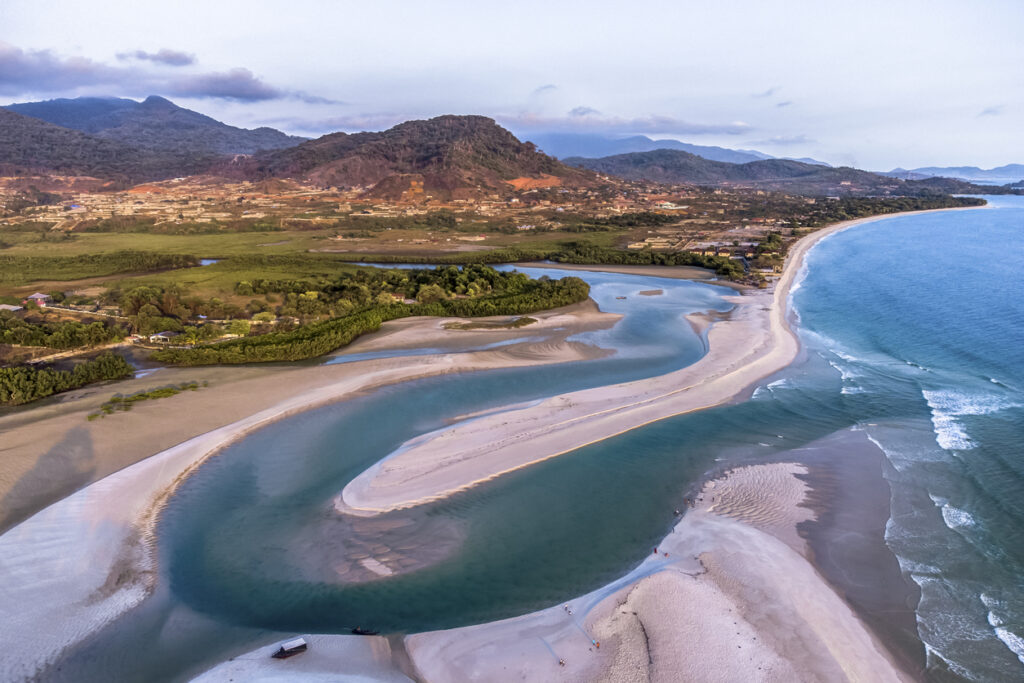 Luftaufnahme einer geschwungenen Flussmündung mit hellen Sandbänken am Ozean in Sierra Leone.