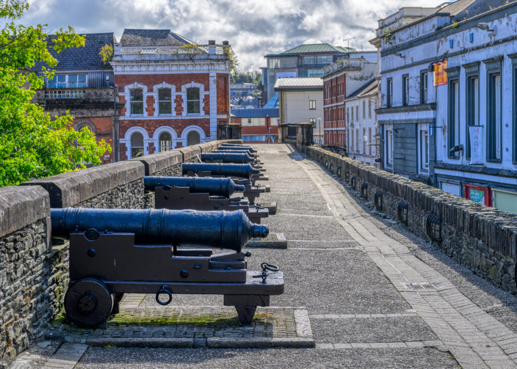 Alte Kanonen stehen entlang der Stadtmauer von Derry zwischen historischen Gebäuden.
