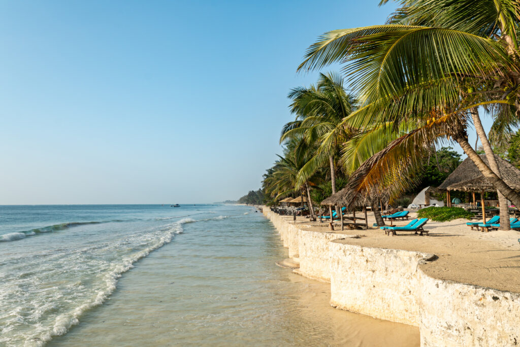 Entlang des Diani Beach in Kenia stehen Palmen, Sonnenliegen und kleine Strandbars direkt am Wasser.