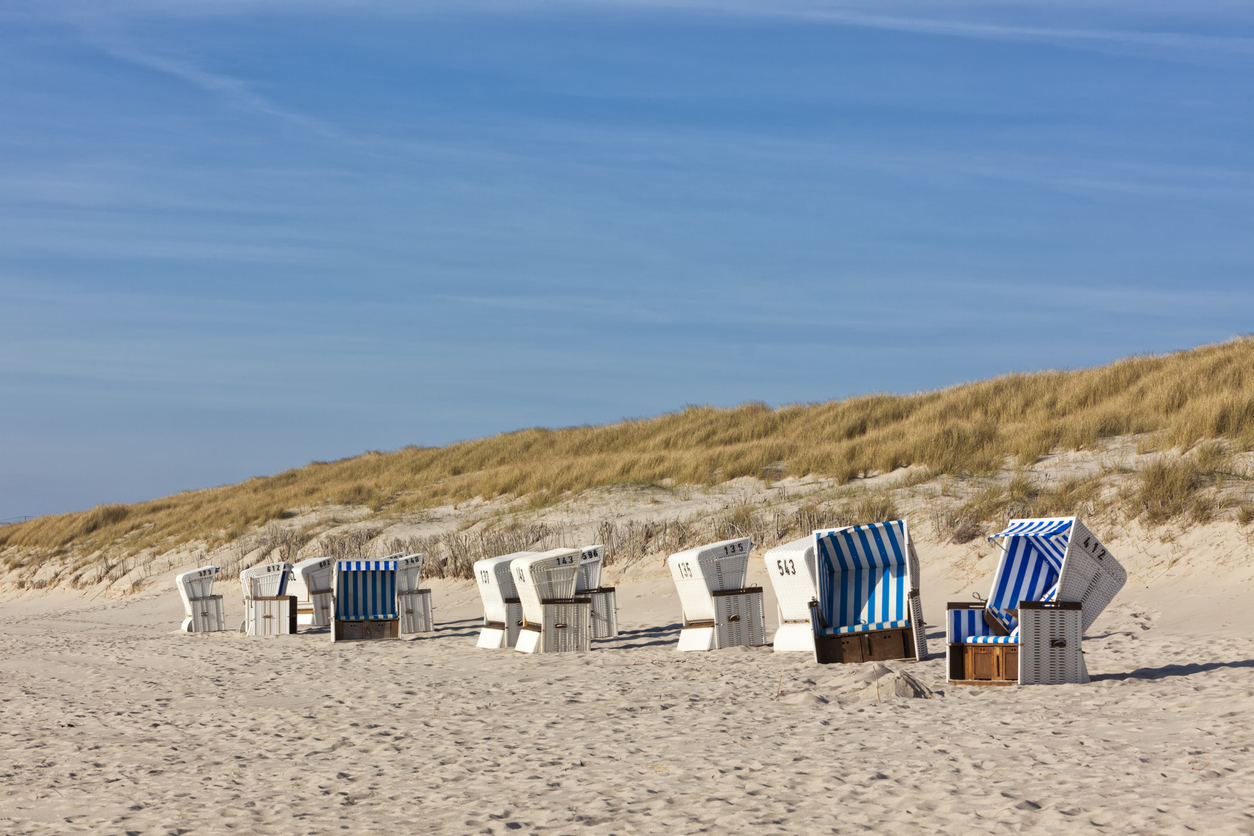 Mehrere Strandkörbe stehen am Strand auf Sylt vor einer Dünenkette.