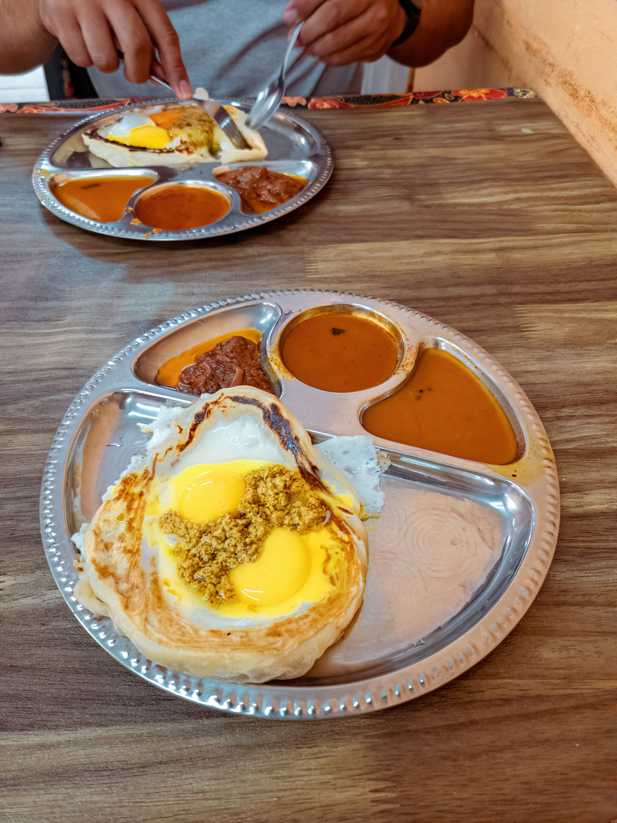 Auf einem Metalltablett liegen Eier im Roti Sarang Burung mit mehreren würzigen Soßen und Beilagen.