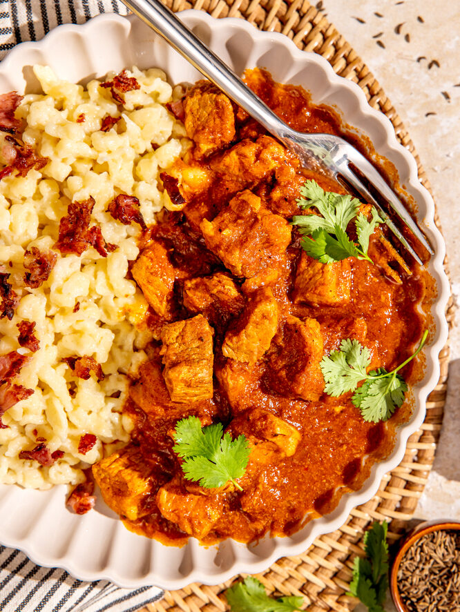 Teller mit ungarischem Pörkölt und cremigen Nockerln, angerichtet mit frischen Kräutern.