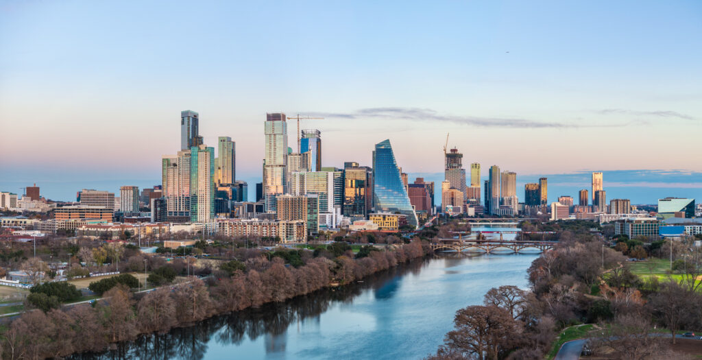 Weitwinkelansicht der Skyline von Austin, Texas, mit modernen Hochhäusern entlang eines breiten Flusses und mehreren Brücken im Nachmittagslicht.