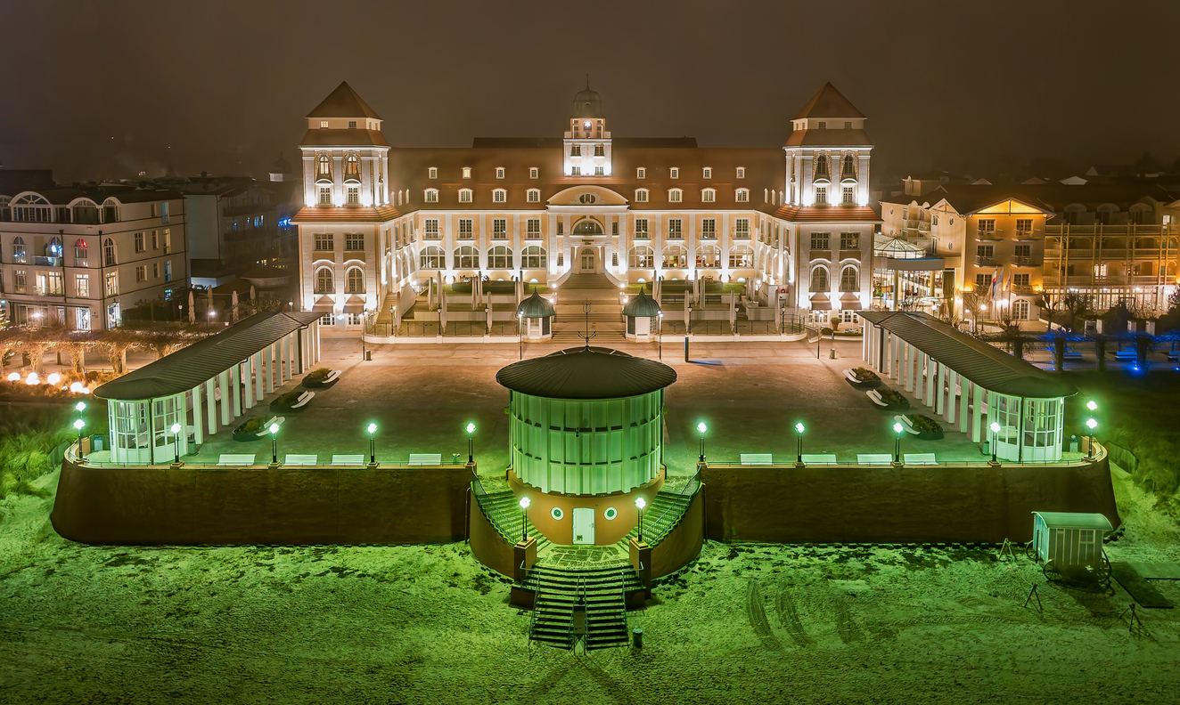 Beleuchtetes Kurhaus von Binz auf Rügen nachts im Winter, umgeben von Schnee und Promenade.