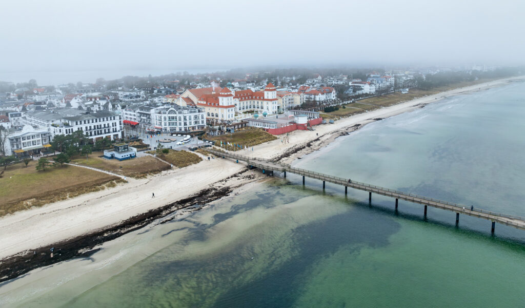 Luftaufnahme von Binz auf Rügen im Winter mit Seebrücke, Strand und leichtem Nebel über der Ostsee.