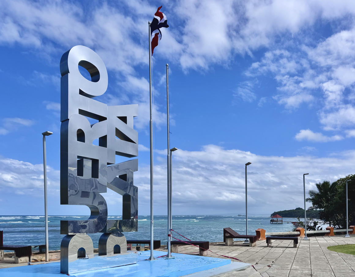 Ein großer Puerto Plata Schriftzug steht an der Küste mit Meerblick und wehender Flagge.