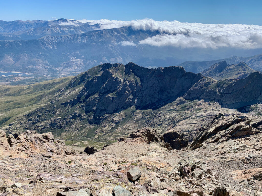 Vom Monte Cinto aus sieht man zerklüftete Felsgrate, weite Täler und Wolkenbänke über den Bergen.