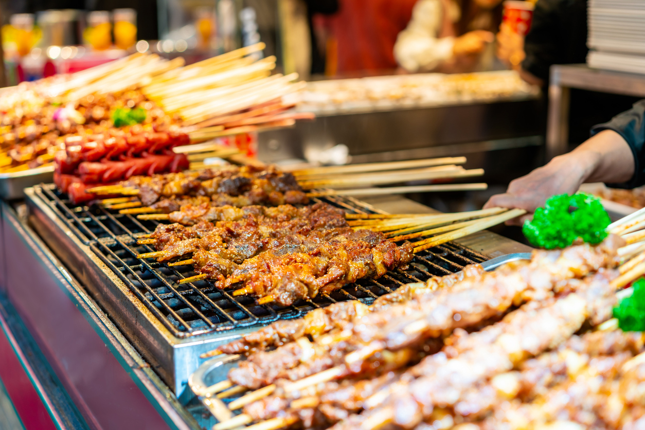 Nahaufnahme von gegrillten Fleischspießen auf einem dampfenden Streetfood-Grill in Chengdu.