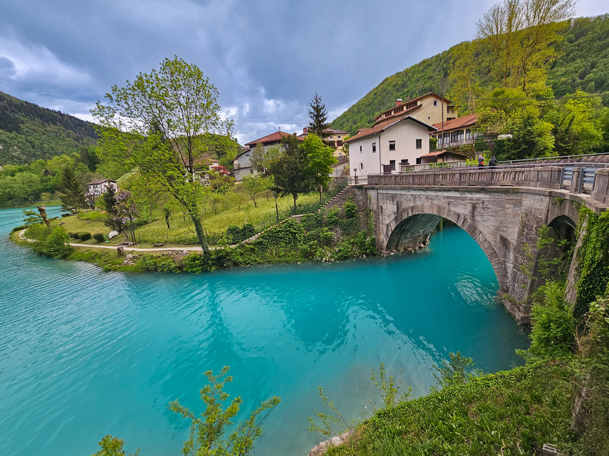 Historische Steinbrücke überspannt den leuchtend türkisgrünen Fluss vor einem kleinen Dorf im Soča-Tal.