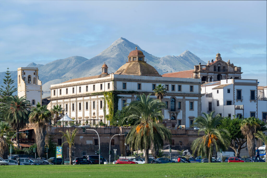 Großes historisches Gebäude in Palermo mit Kuppeldach und Bergen im Hintergrund.