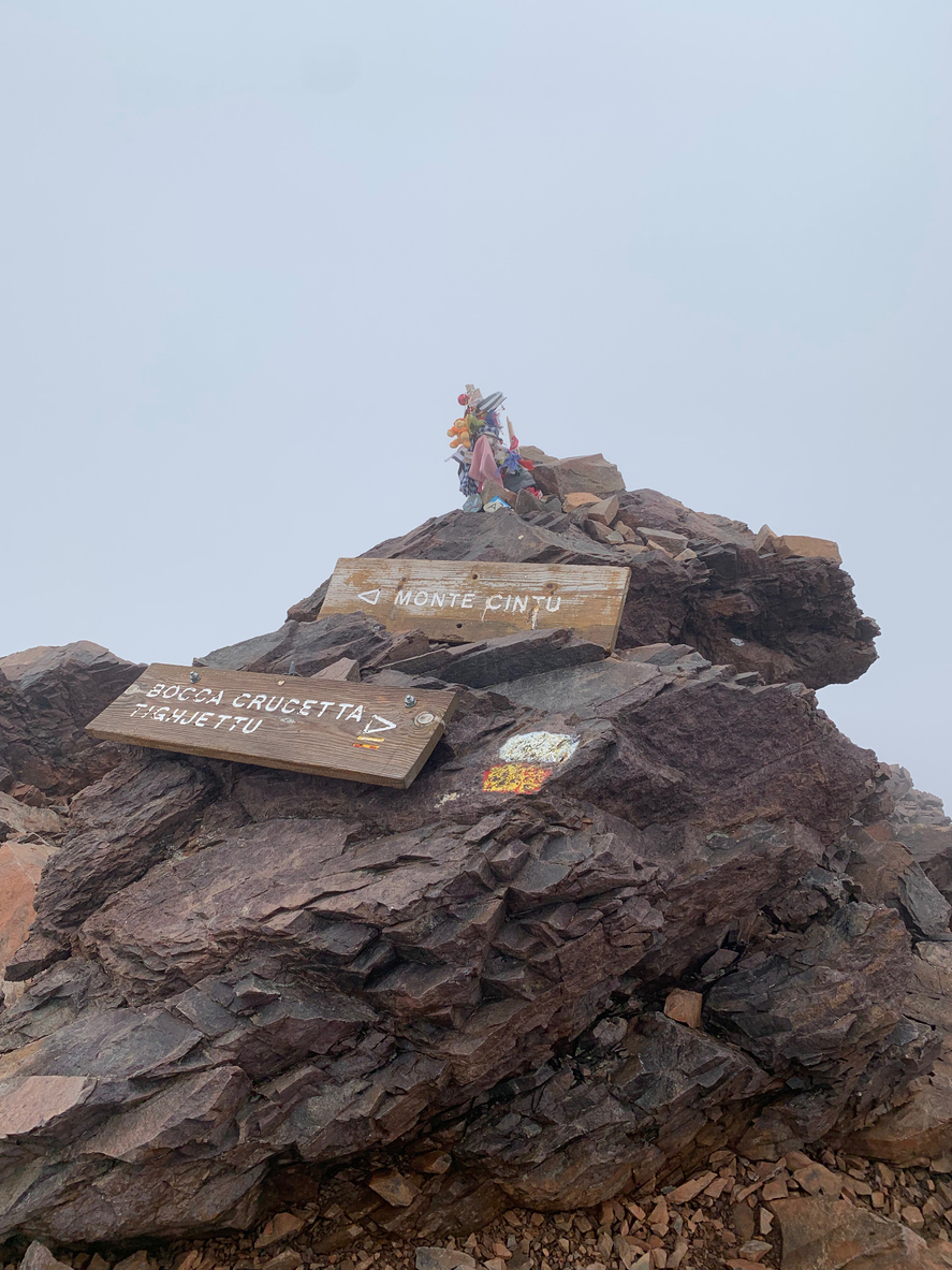 Auf einem felsigen Grat stehen Holzschilder mit der Aufschrift Monte Cinto und Bocca Crucetta am GR20.