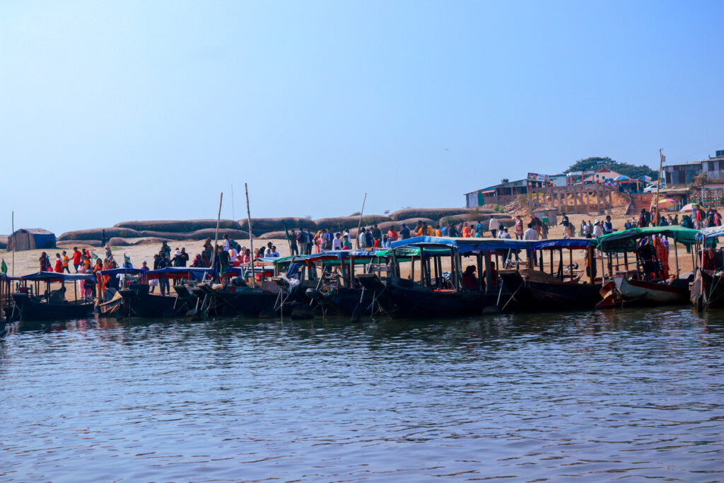 Menschen steigen in Sylhet an einem Sandufer in bunte Holzboote am Fluss ein.