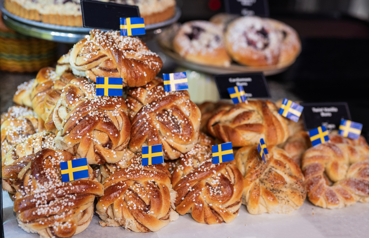 Ein Stapel schwedischer Zimtschnecken mit Hagelzucker und kleinen Schwedenfähnchen auf einem Tisch.