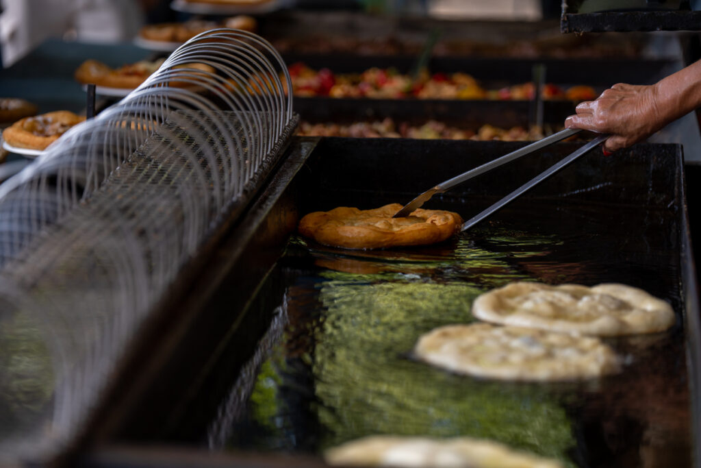 Hand wendet einen goldbraunen Lángos in heißem Fett in einer Fritteuse.