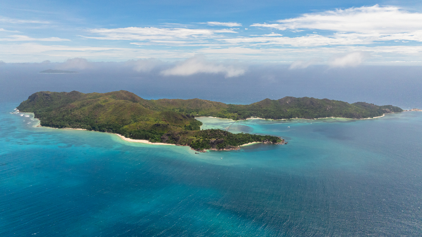 Luftaufnahme der Insel Curieuse mit grünen Hügeln, hellen Stränden und türkisfarbenem Meer.