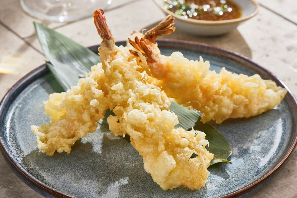 Drei goldbraune Tempura-Garnelen liegen auf einem Teller mit Dip in einem Restaurant in Tokio.