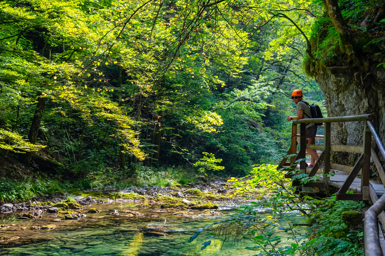 Wanderin mit Helm steht auf einem Holzsteg über dem türkisgrünen Wasser der Vintgar-Schlucht in Slowenien.