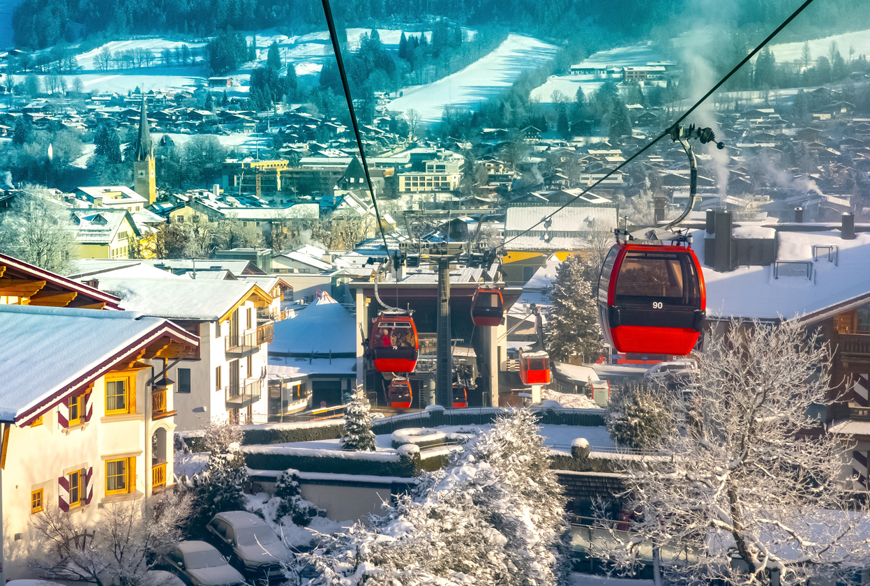 Rote Gondelbahn fährt über das verschneite Kitzbühel mit Blick auf die Dächer der Stadt.