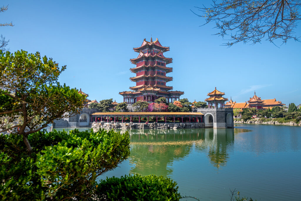 Mehrstöckiger Pagodenturm mit roten Fassaden und goldenen Dächern steht in Xi’an an einem ruhigen See, umgeben von Gartenanlagen.