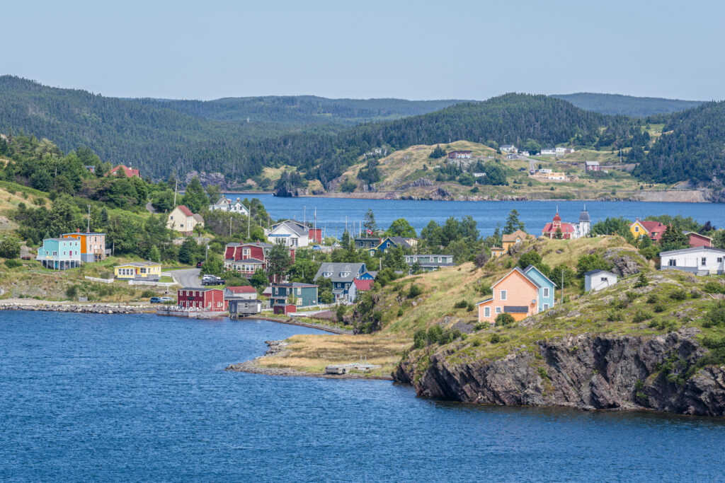 Blick auf die farbenfrohen Holzhäuser von Trinity in Neufundland an einer geschützten Bucht mit bewaldeten Hügeln im Hintergrund.