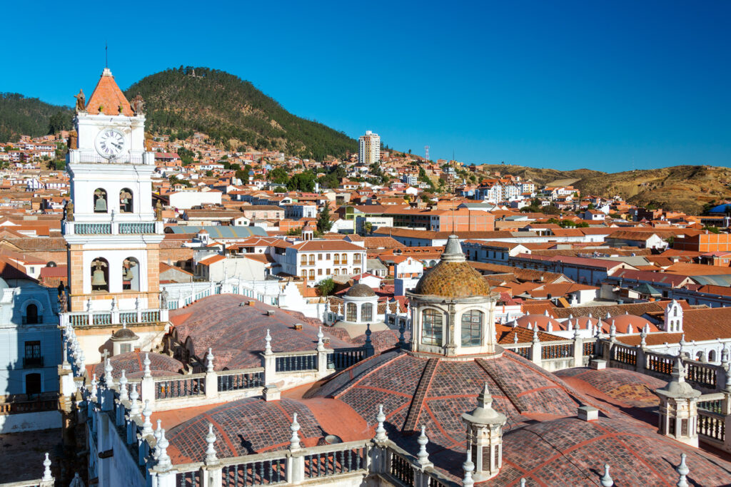 Panorama über Sucre in Bolivien mit Kirchturm, Kuppel und roten Dächern vor Bergen.