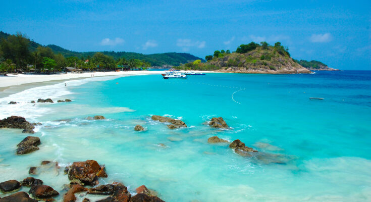 Auf Redang leuchtet das Meer in kräftigem Türkis, während Felsen und ein heller Sandstrand die Bucht säumen.