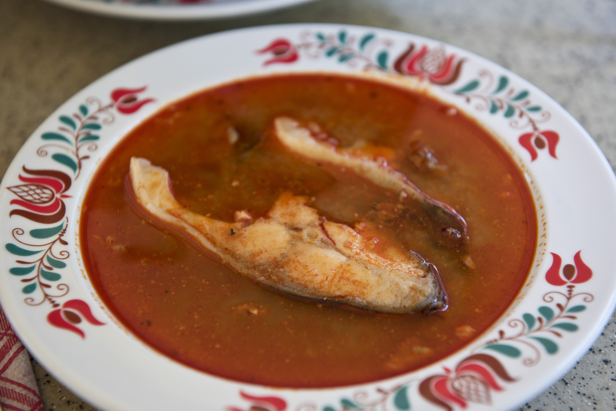 Teller mit roter Halászlé und einem Stück Fischfilet in der Mitte.