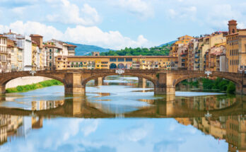 Historische Steinbrücken und Häuser spiegeln sich im Arno im Zentrum von Florenz.