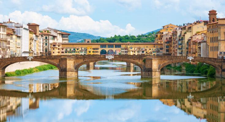 Historische Steinbrücken und Häuser spiegeln sich im Arno im Zentrum von Florenz.
