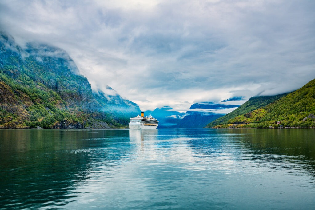 Ein Kreuzfahrtschiff fährt auf dem Hardangerfjord in Skandinavien durch ein Tal aus grünen Bergen und Wolken.