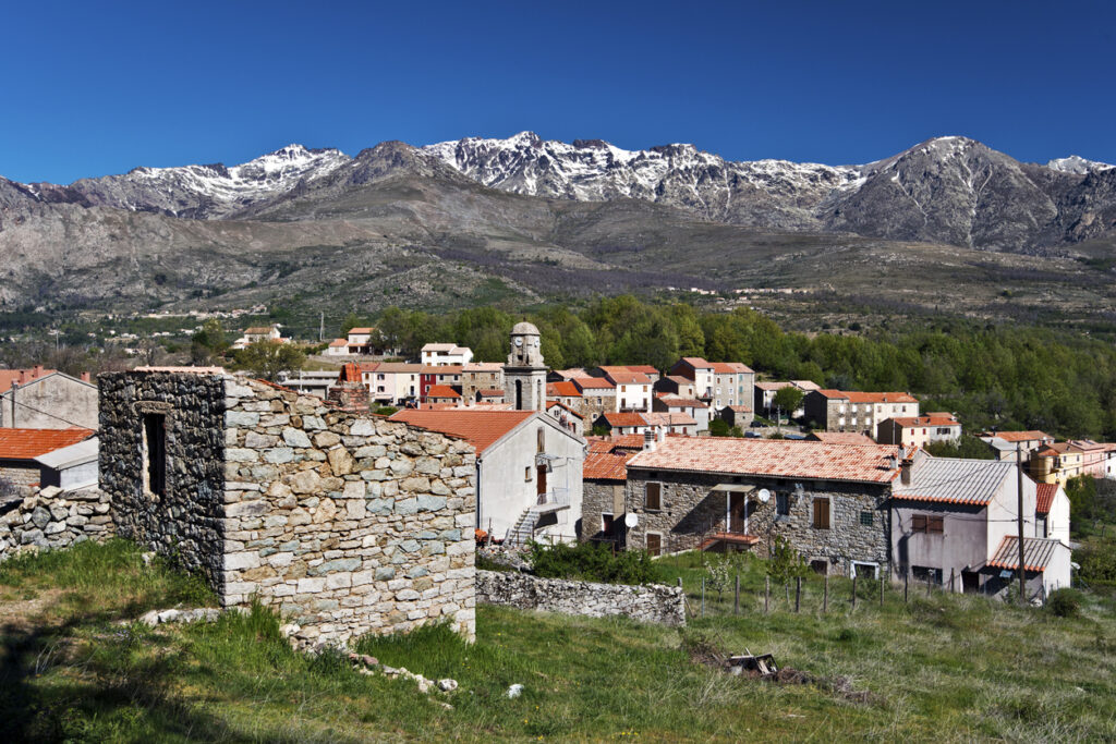 Ein korsisches Dorf mit roten Dächern liegt vor schneebestäubten Bergen des Monte-Cinto-Massivs.