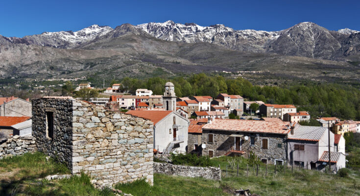 Ein korsisches Dorf mit roten Dächern liegt vor schneebestäubten Bergen des Monte-Cinto-Massivs.