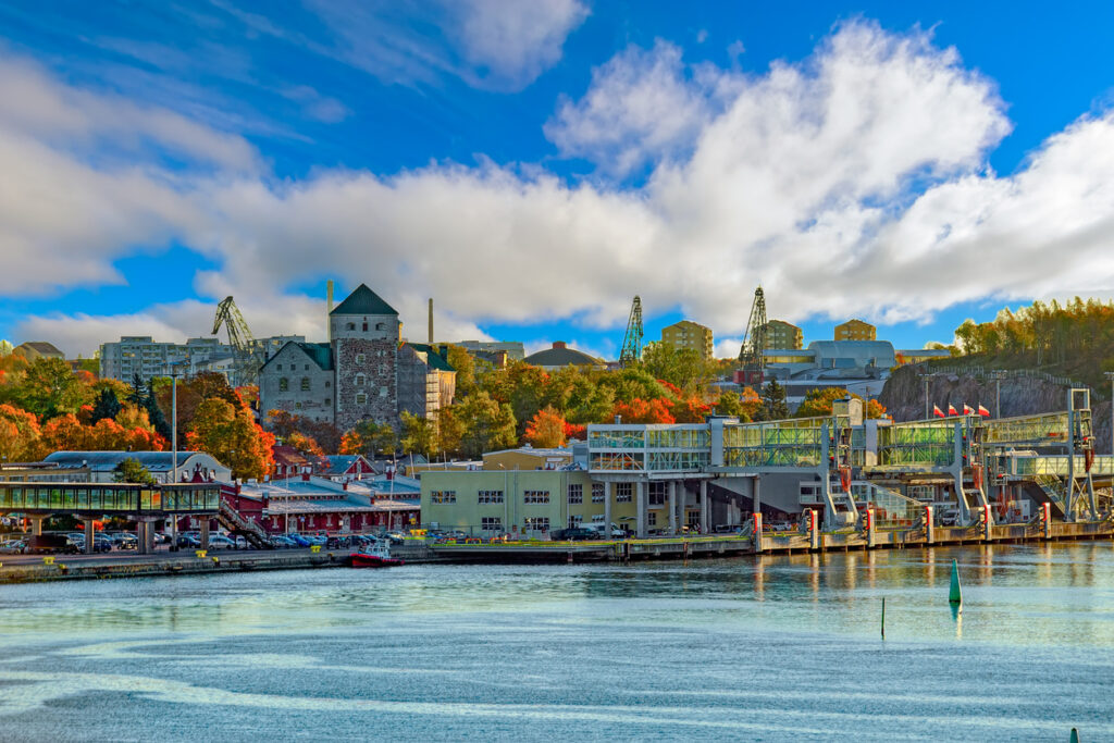 Blick über den Hafen von Turku mit Burg und farbigen Herbstbäumen im Hintergrund.