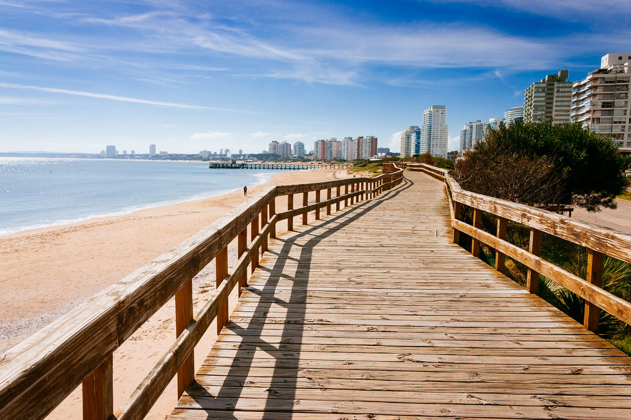 Langer Holzsteg über dem Sandstrand mit Blick auf die Hochhäuser von Punta del Este.