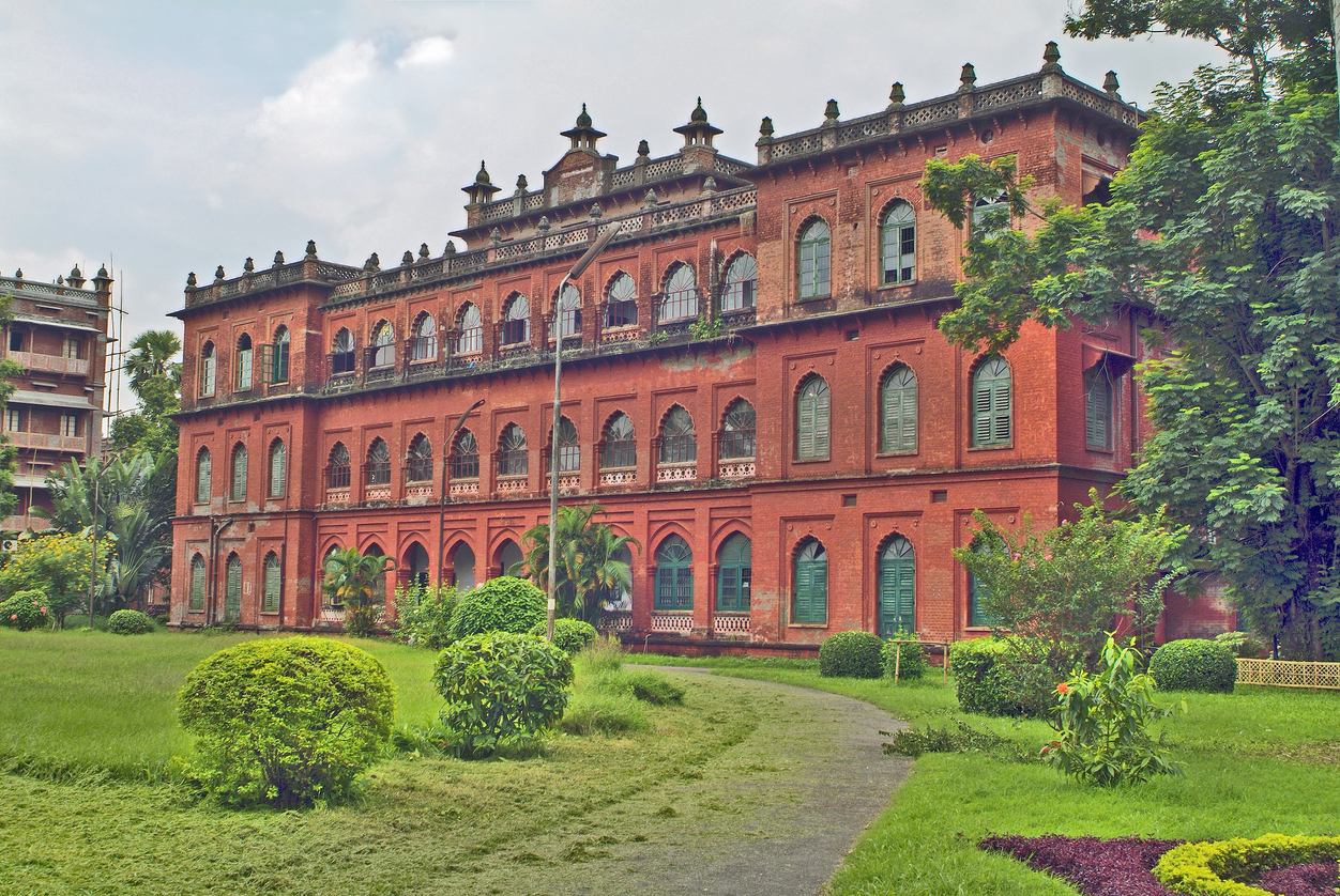 Rotes historisches Gebäude mit grünen Fensterläden in einem Garten in Dhaka.