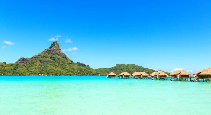 Überwasser-Bungalows vor grünem Berg in der Lagune von Französisch-Polynesien.