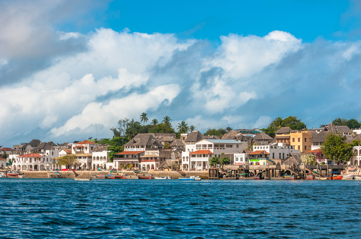 Blick vom Wasser auf die Altstadt von Lamu, Kenia mit bunten Häusern und kleinen Booten.