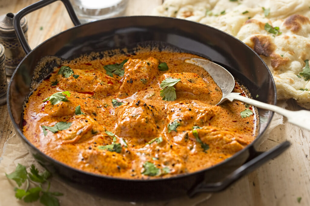 Butter Chicken mit zarten Hähnchenstücken in cremiger orangefarbener Sauce, garniert mit Koriander.