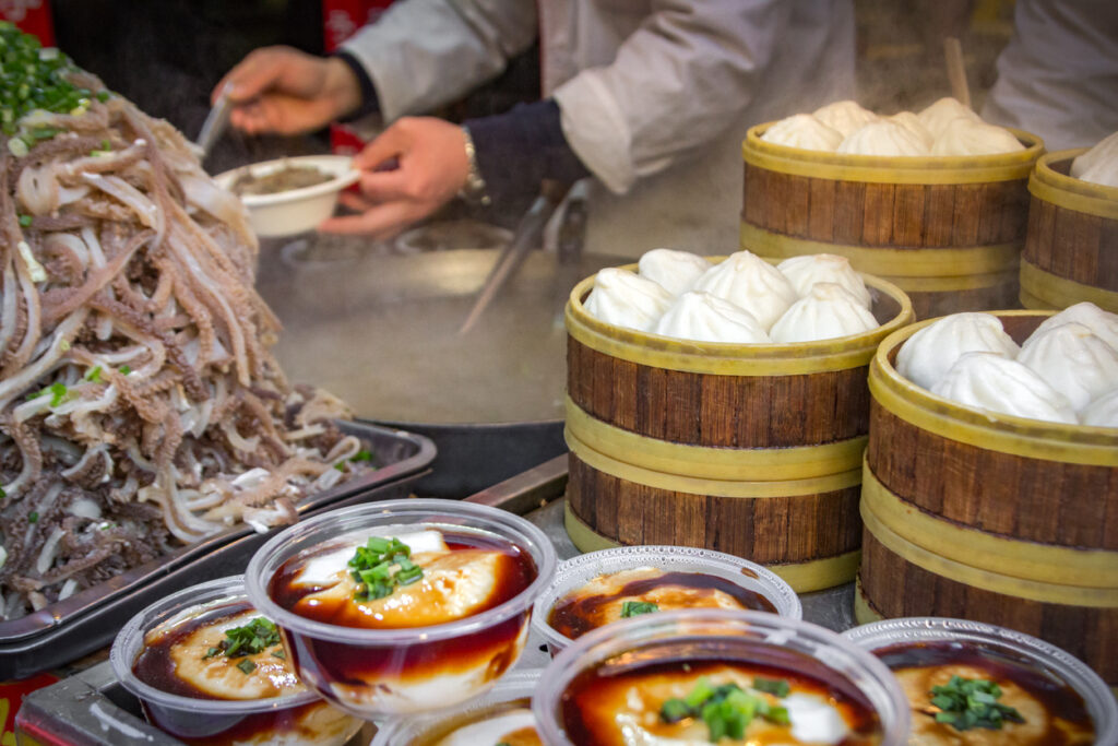 Straßenstand in Peking mit gedämpften Teigtaschen und Schalen mit Tofugericht.