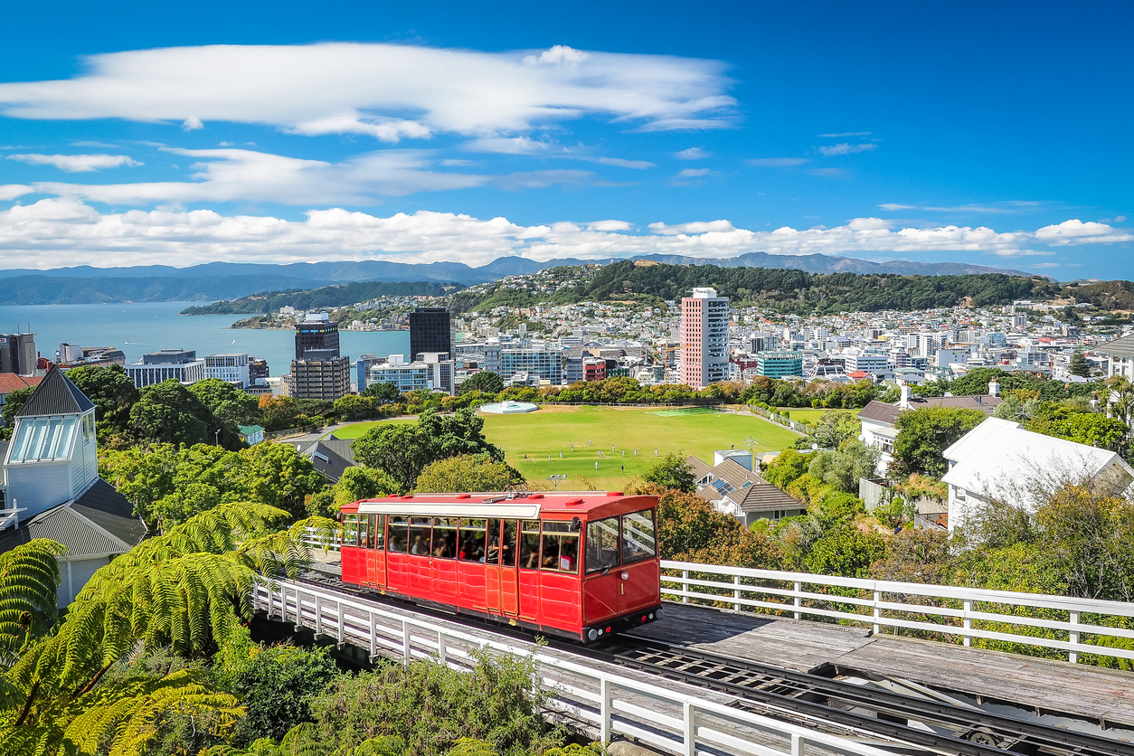 Rote Cable Car in Wellington fährt über die Schienen mit Blick auf Stadt, Hügel und Hafen.