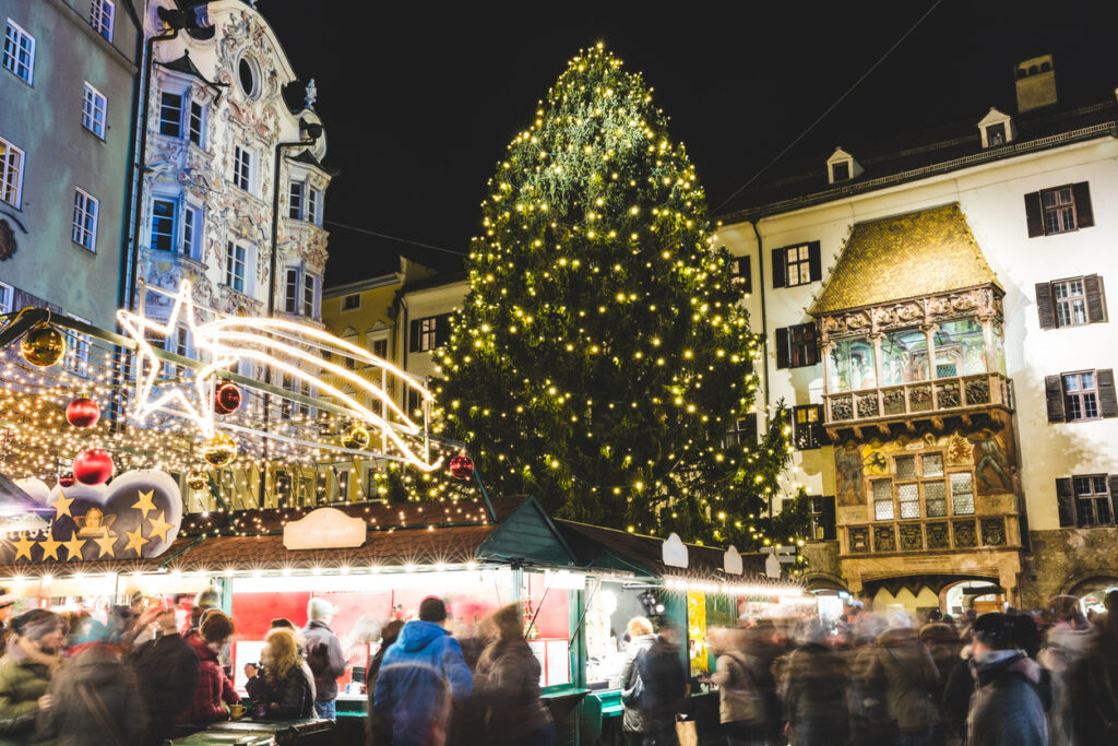 Stimmungsvoller Weihnachtsmarkt in Innsbruck mit großem Weihnachtsbaum und dem Goldenen Dachl im Hintergrund.
