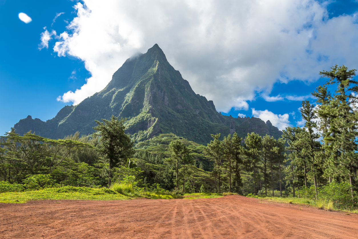Markanter grüner Berg ragt in Französisch-Polynesien über dichtem Regenwald in den blauen Himmel.
