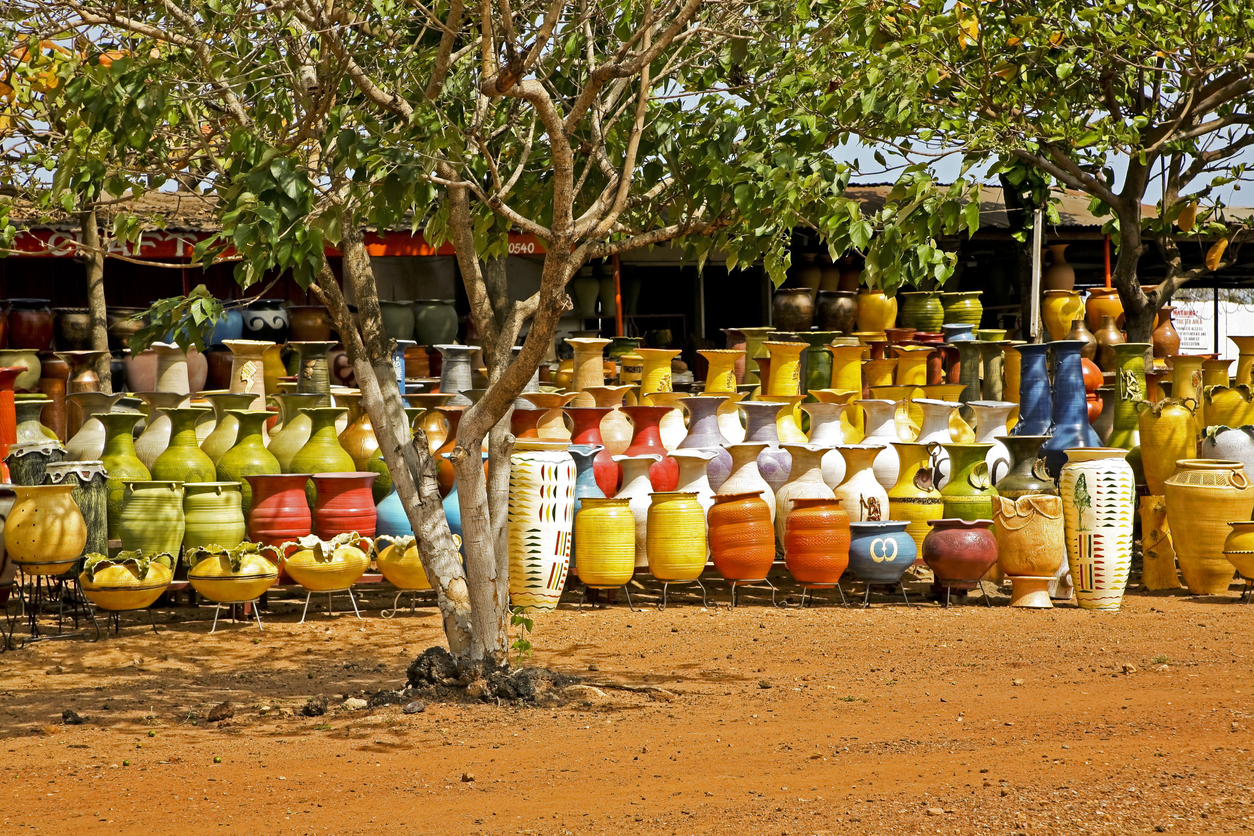 Zahlreiche farbenfrohe Keramiktöpfe stehen dicht an dicht unter Bäumen auf einem Markt in Ghana.
