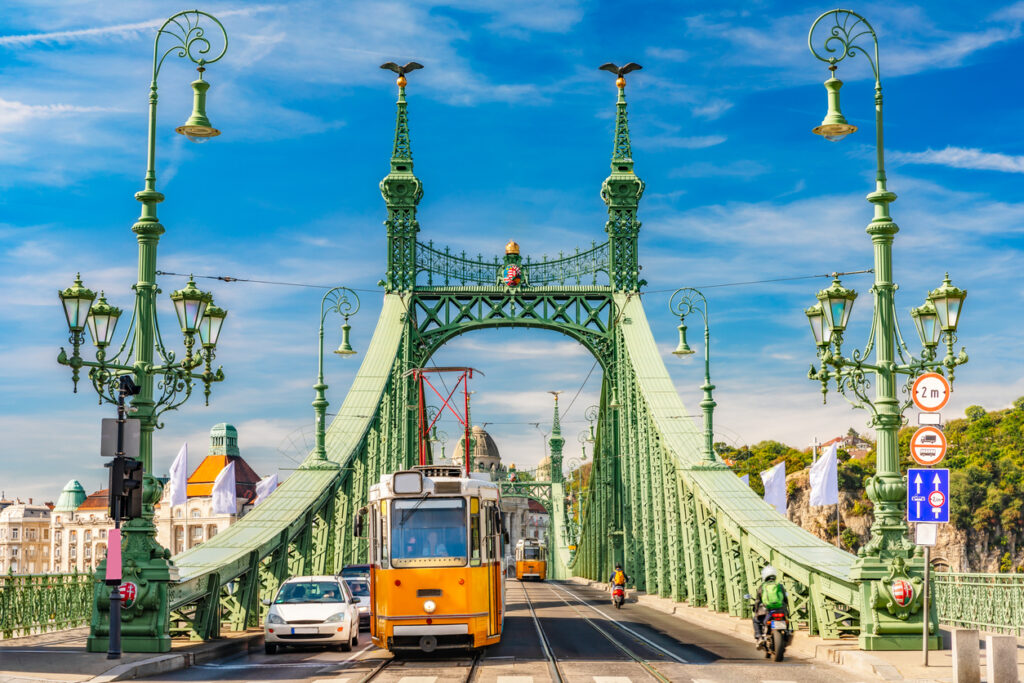 Eine gelbe Straßenbahn fährt über die grüne Freiheitsbrücke in Budapest.