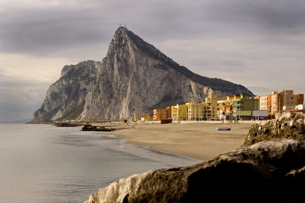 Ein Strand in Gibraltar liegt vor der Küste, dahinter dominiert der Felsen die Skyline.